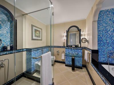 Modernes Badezimmer mit blauen Mosaikfliesen, Dusche, Waschbecken und Badewanne bei warmem Licht.