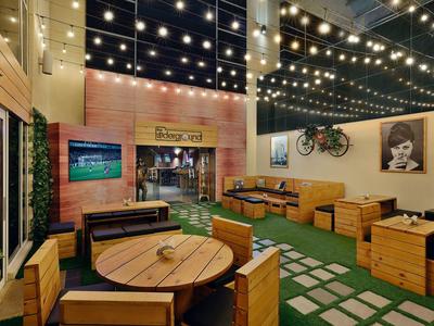 Gemütliche Lounge mit Holzmöbeln, grünen Pflanzen, Lichterketten und Wanddekoration.