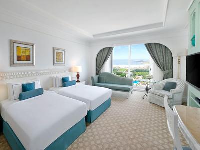 Hell eingerichtetes Hotelzimmer mit zwei Einzelbetten, Sesseln und großem Fenster mit Blick.
