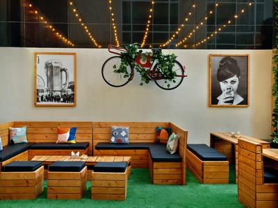 Gemütliche Holzbank mit schwarzen Kissen, grüner Wand und Fahrrad-Deko in modernem Café-Außenbereich.