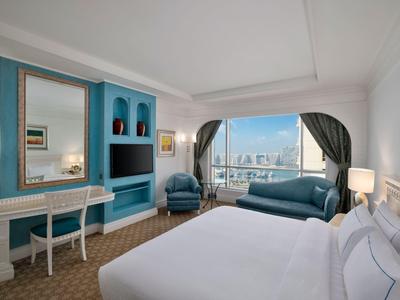 Heller Hotel-Zimmer mit großem Bett, Sitzbereich und Blick auf die Stadt durch Fenster.