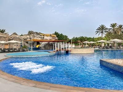 Großer Hotelpool mit Sonnenschirmen, Liegen und Wasserrutschen bei Sonnenuntergang.