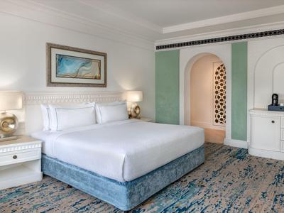 Hell eingerichtetes Hotelzimmer mit großem Bett, Teppichboden und dekorativem Bogen.