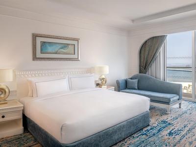 Helles Hotelzimmer mit großem Bett, Sofa und Meerblick durch große Fenster.