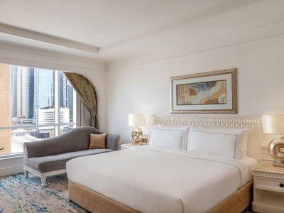 Modernes Hotelzimmer mit großem Bett, Sitzbank, Kunst an der Wand und Blick auf Hochhäuser.