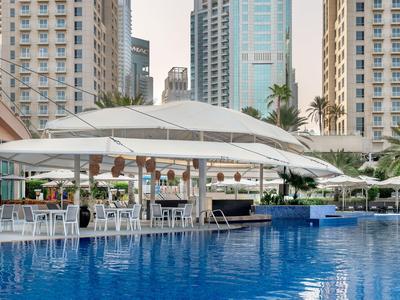 Poolbereich mit großen weißen Sonnenschirmen zwischen hohen Gebäuden in der Stadt.