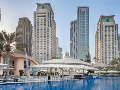 Moderne Hochhäuser und ein luxuriöser Poolbereich mit Liegestühlen und Palmen in einer Hotelanlage.