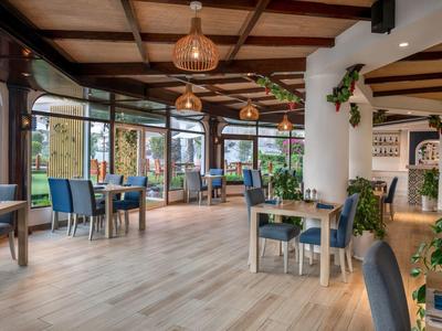 Hell eingerichteter Speisesaal mit Holzbalkendecke, Tischsets und Stühlen mit blauen und grauen Bezügen.