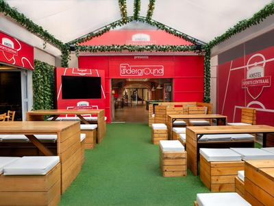 Moderner Innenbereich mit Holzmöbeln, grüner Teppichboden und roter Wandgestaltung in einem Hotelrestaurant.