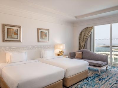 Helles Hotelzimmer mit zwei Einzelbetten, Sitzbereich und Balkon mit Meerblick.