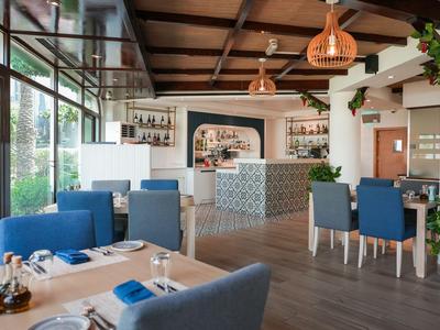 Helles Hotelrestaurant mit blauen Stühlen, Holzboden und großer Fensterfront.
