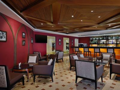 Hotelbar mit gemütlichen Sesseln, roter Wand und beleuchtetem Tresen unter Holzdecke.