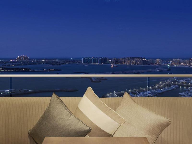 Bequeme Kissen in neutralen Tönen auf beige Sofa mit Meerblick und Stadtlichtern im Hintergrund bei Nacht.