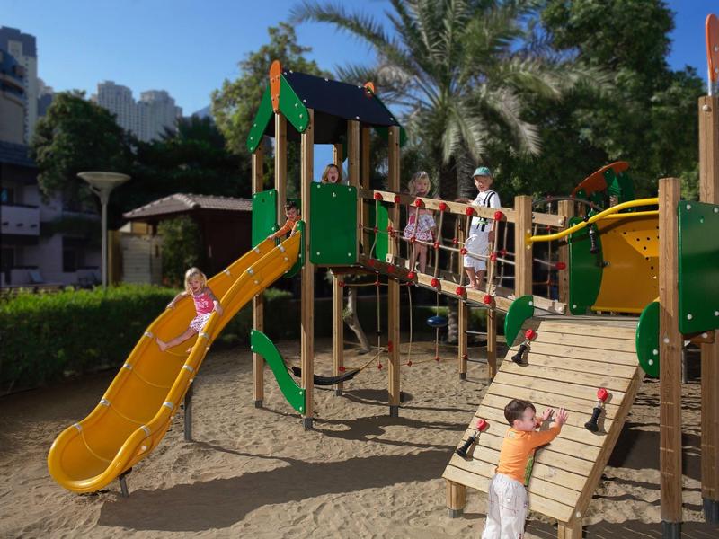 Kinderspielplatz mit gelber Rutsche, Klettergerüst und mehreren spielenden Kindern an einem sonnigen Tag.
