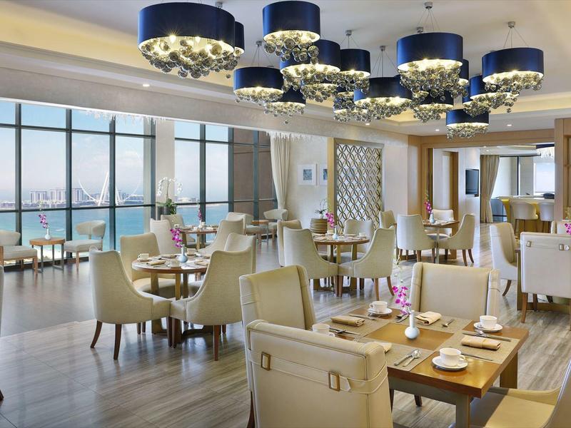 Helles, modernes Restaurant mit großen Fenstern, cremefarbenen Sesseln und blauen Hängeleuchten.