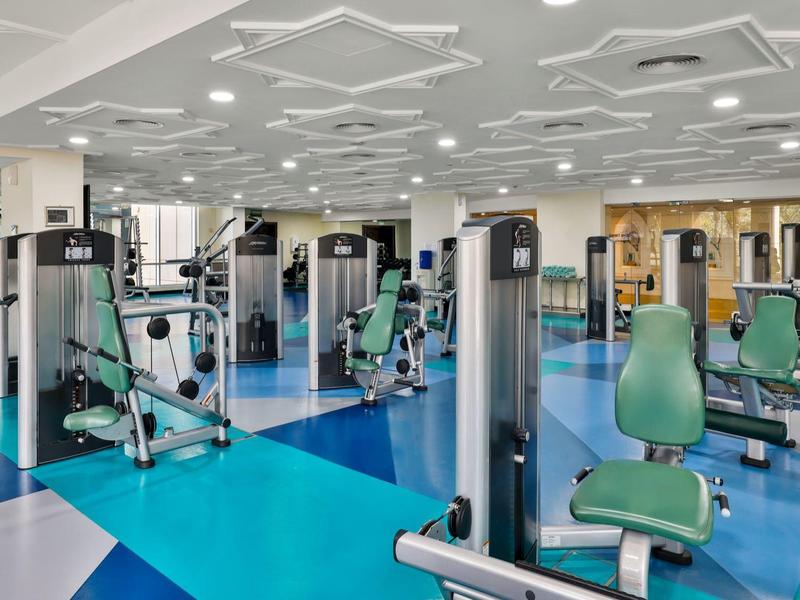 Moderner Fitnessraum mit blauen und grauen Bodenfliesen, weißen Wänden und verschiedenen Trainingsgeräten.