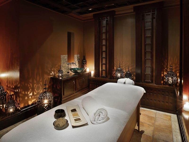 Gemütlicher, dunkler Massageraum mit weißer Liege, gedämpftem Licht und entspannender Dekoration.