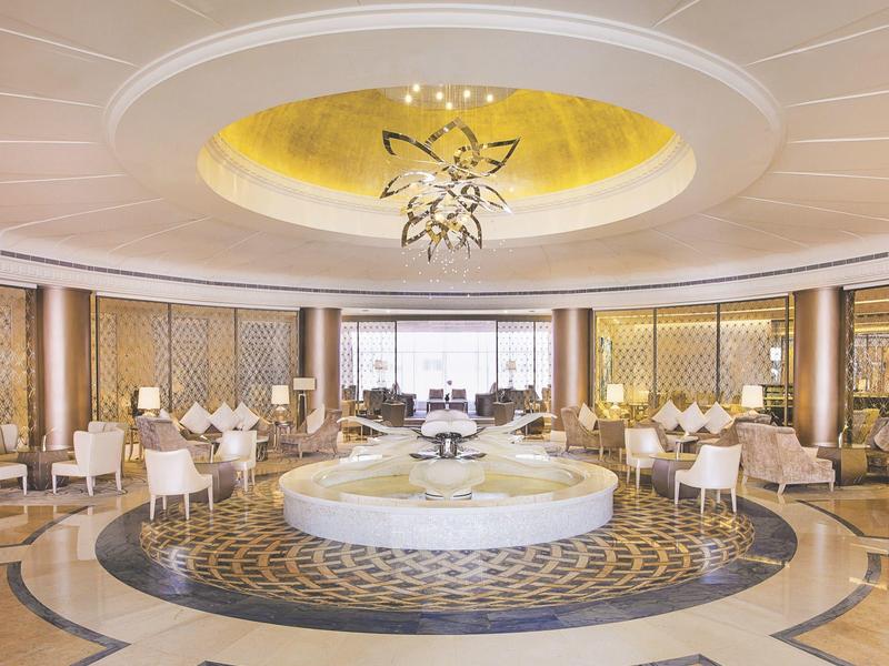 Eleganter runder Speisesaal mit hellen Stühlen, goldenen Wänden und einem großen Kronleuchter.