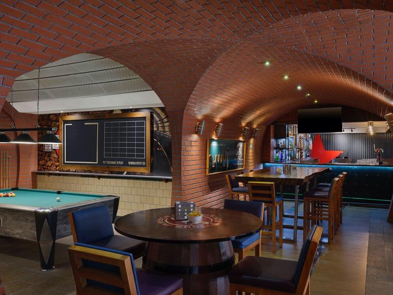 Gemütliche Bar mit rundem Holztisch, Pooltisch und gewölbter roter Backsteinwand.