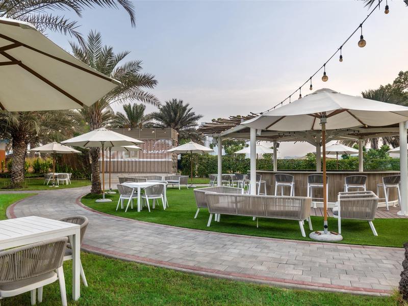 Freiluftbereich mit weißen Tischen, Stühlen und Sonnenschirmen auf Rasen und gepflastertem Weg