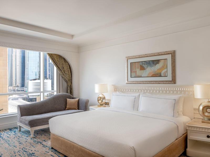 Modernes Hotelzimmer mit großem Bett, Sitzbank, Kunst an der Wand und Blick auf Hochhäuser.