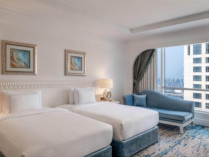 Modernes Hotelzimmer mit zwei Betten, Sofalandschaft und großem Fenster mit Blick auf die Stadt.