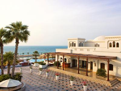 Hotel mit weißem Gebäude, Palmen und Meer im Hintergrund bei Tageslicht.