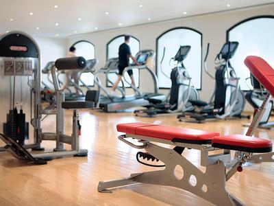 Moderner, gut beleuchteter Fitnessraum mit Laufbändern, Kraftgeräten und roten Polsterbänken.