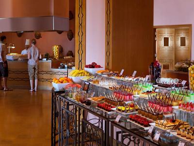Buffet mit vielfältigen Speisen und Getränken, helle Holzmöbel, Gäste im Hintergrund.