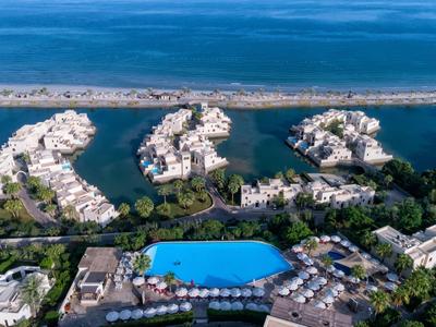 Luftaufnahme einer Küstenanlage mit türkisfarbenem Pool, Wohnhäusern und Brücken im Meer.