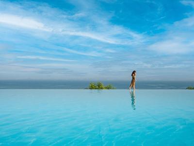 Unendlicher Pool mit klarem blauem Wasser, darüber weite Wolken am Himmel, Person im Hintergrund.