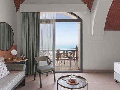 Helles Wohnzimmer mit grauem Sofa, runden Spiegel, Sessel und Blick auf Terrasse mit Meer.