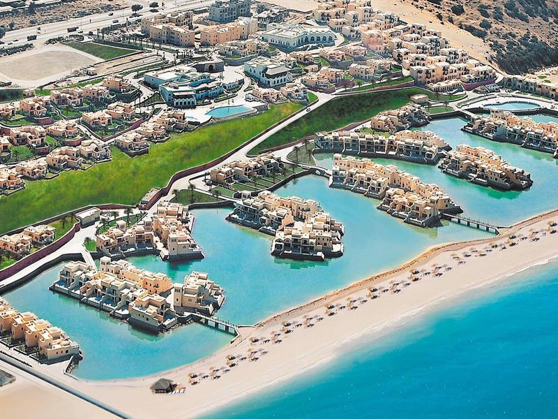 Luxusresort mit Villen auf künstlichen Inseln, strahlend blauem Wasser und einem langen Sandstrand.