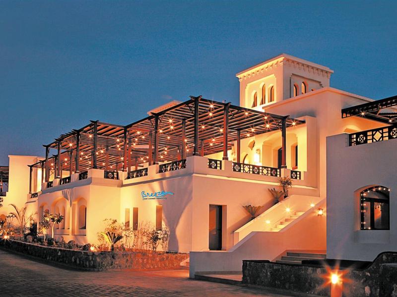 Weißes Gebäude mit Treppe und Terrasse bei Abenddämmerung, beleuchtet mit warmem Licht.