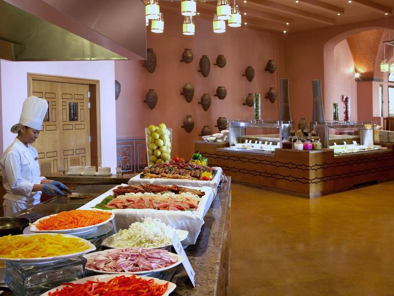 Restaurantbuffet mit bunten Gerichten, Haushandwerkerin in weißer Uniform, warme Beleuchtung.