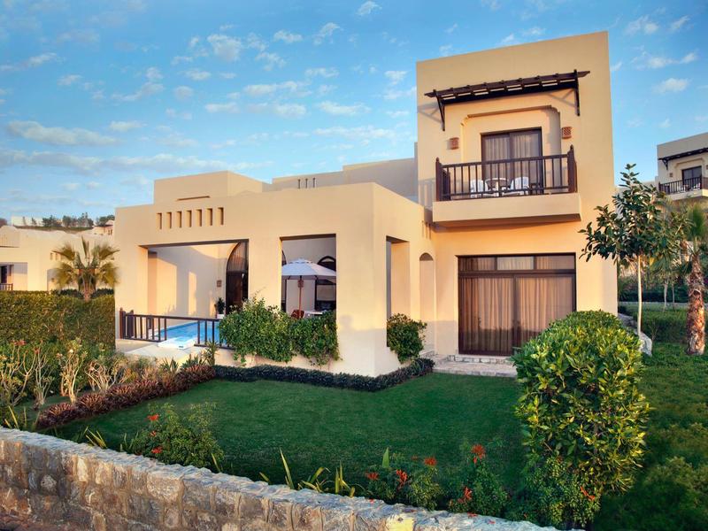 Modernes zweistöckiges Haus mit Balkon, großem Garten und grünem Rasen unter blauem Himmel.