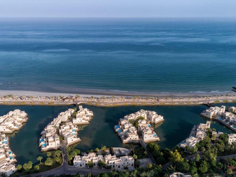 Luftaufnahme von Inselresorts mit weißen Gebäuden an einem blauen Meer und einem Sandstreifen.
