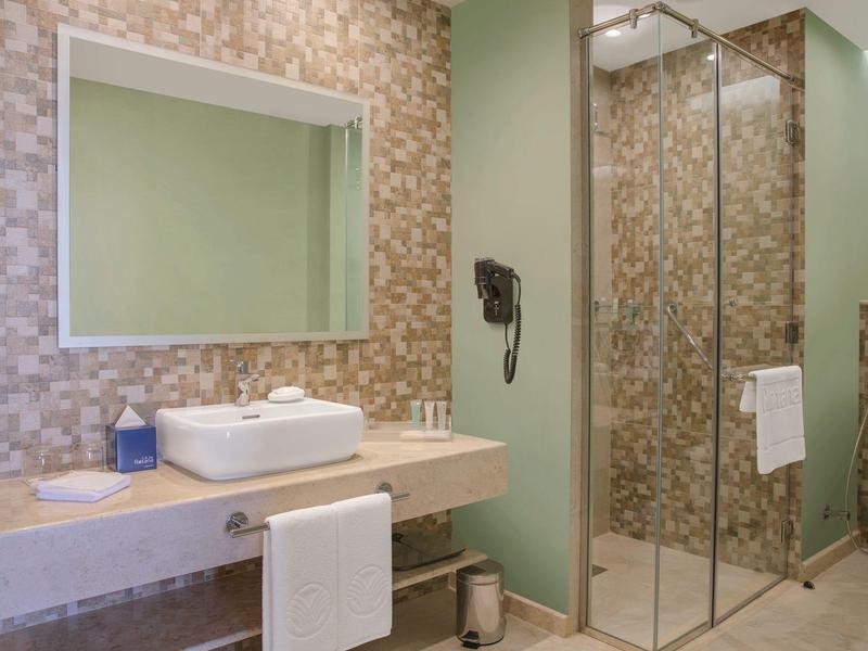 Moderner Badezimmerbereich mit Waschtisch, großem Spiegel und begehbarer Glasdusche, helle Fliesen.