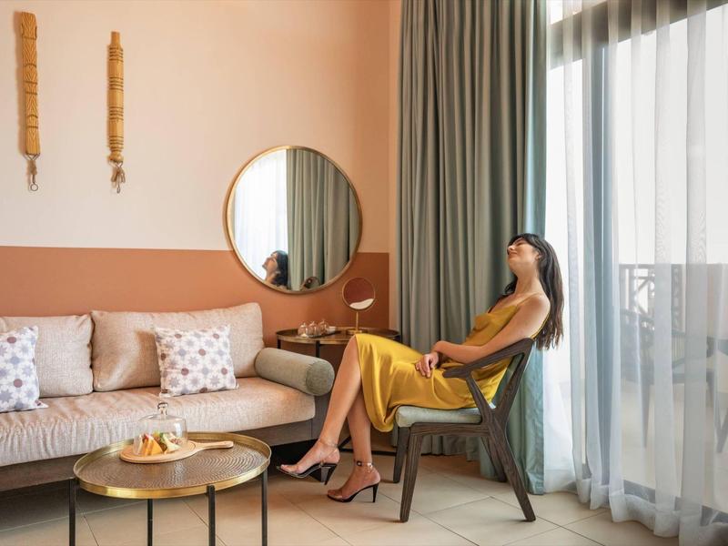 Frau entspannt sich im Wohnzimmer eines Hotels neben Balkon mit Vorhängen.