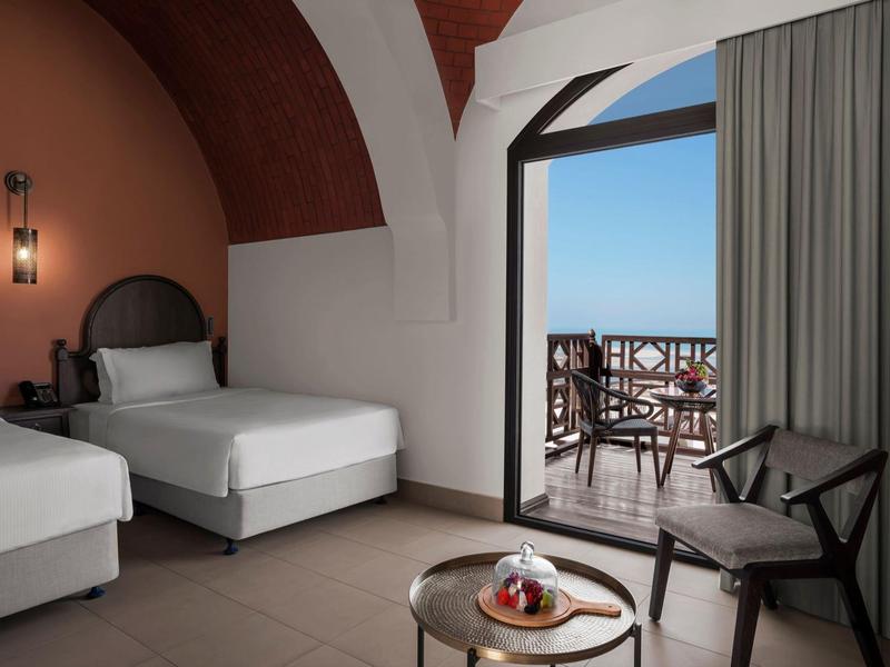 Moderner Hotelraum mit zwei Einzelbetten, kleinem Tisch, Stuhl und Balkon mit Meerblick.