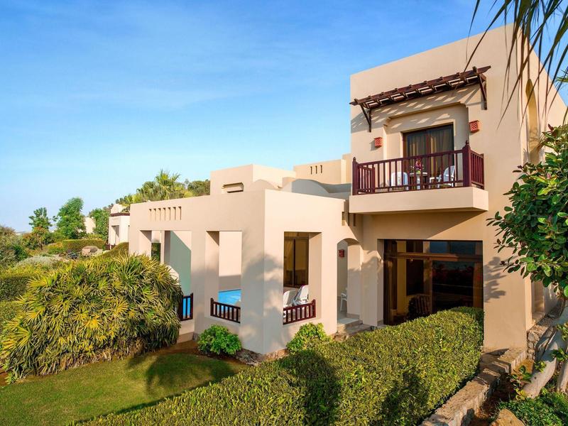 Modernes, zweistöckiges Haus in warmen Beige- und Brauntönen mit Garten und klarem Himmel.