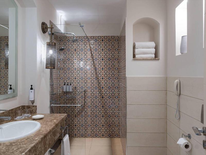 Moderner Badezimmerspiegel, Waschbecken mit braunem Marmor, Dusche mit gemusterten Fliesen.