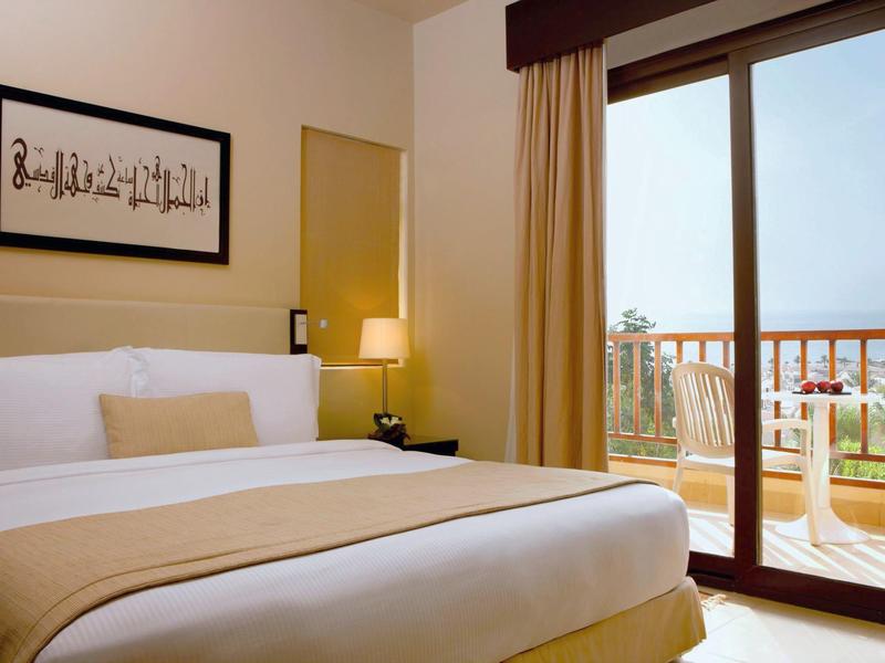 Hell eingerichtetes Schlafzimmer mit großem Bett, Lampe, Kunst an der Wand und Balkon mit Glas-Schiebetür.