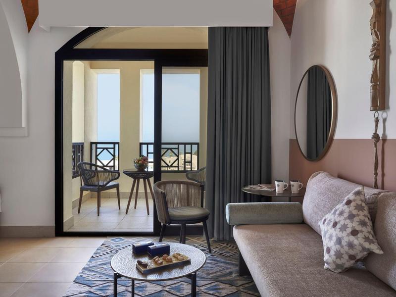 Modernes Wohnzimmer mit grauem Sofa, rundem Spiegel, Teppich und Zugang zu Balkon mit Stühlen.