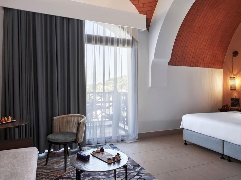 Modernes Hotelzimmer mit weißem Bett, dunklen Vorhängen und rotem Gewölbedeckenbogen.