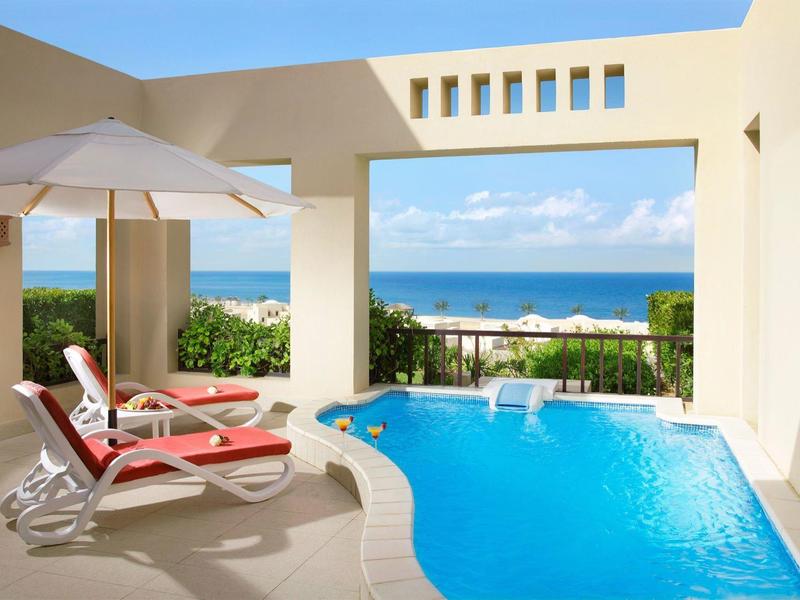 Pool auf Terrasse mit zwei roten Liegestühlen und Blick auf das Meer unter blauem Himmel.