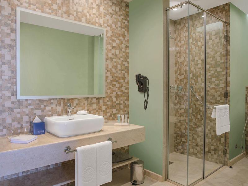 Modernes Hotelbad mit Waschbecken, Spiegel, Haartrockner und Dusche mit Glaswand.