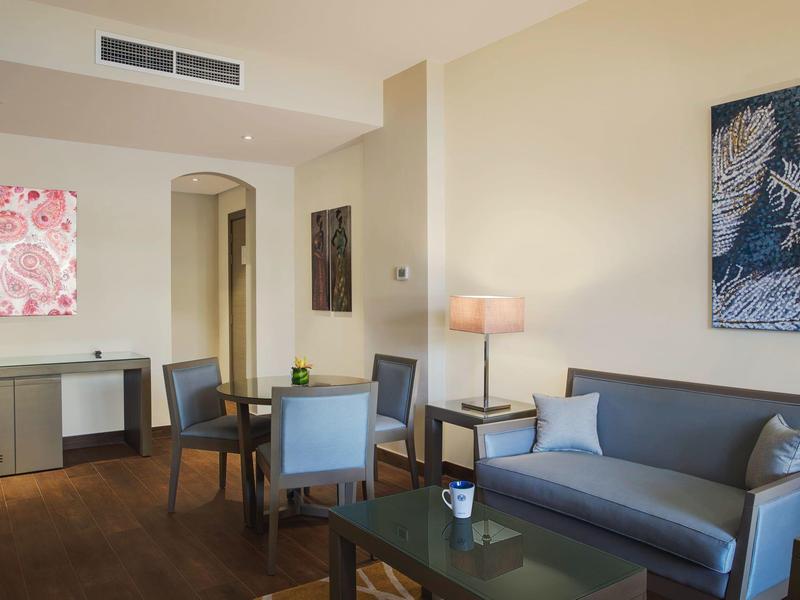 Modern eingerichtetes Hotelzimmer mit Sofa, Esstisch und stilvoller Dekoration an den Wänden.