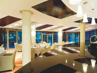 Modernes Hotelrestaurant mit weißen Stühlen, großen Fenstern und warmem Ambiente bei Dämmerung.