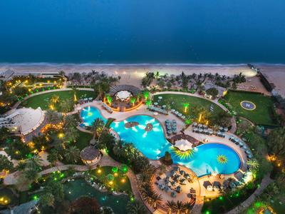 Luftaufnahme eines beleuchteten Hotelpools am Strand bei Nacht